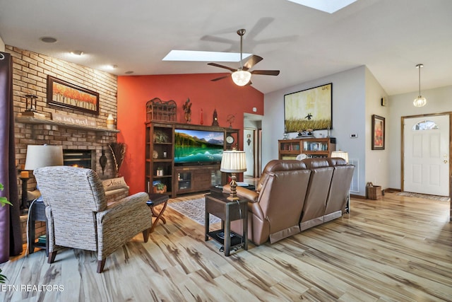 living room with a brick fireplace, light wood-type flooring, lofted ceiling with skylight, and ceiling fan