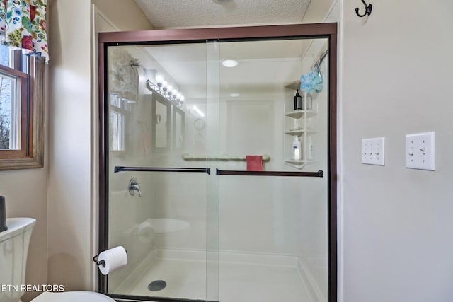 bathroom featuring toilet, a shower with shower door, and a textured ceiling