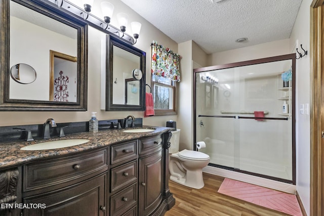 bathroom featuring wood-type flooring, a textured ceiling, an enclosed shower, toilet, and vanity