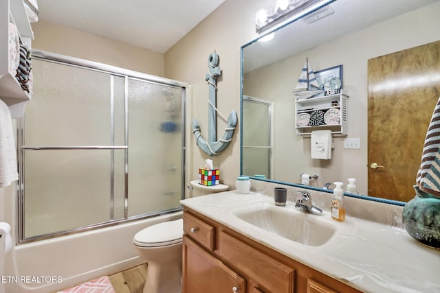 full bathroom featuring combined bath / shower with glass door, hardwood / wood-style floors, vanity, and toilet