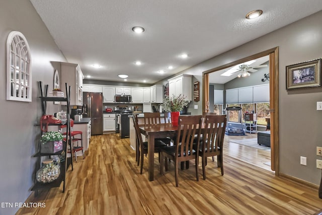 dining room with a textured ceiling, light hardwood / wood-style floors, vaulted ceiling, and ceiling fan