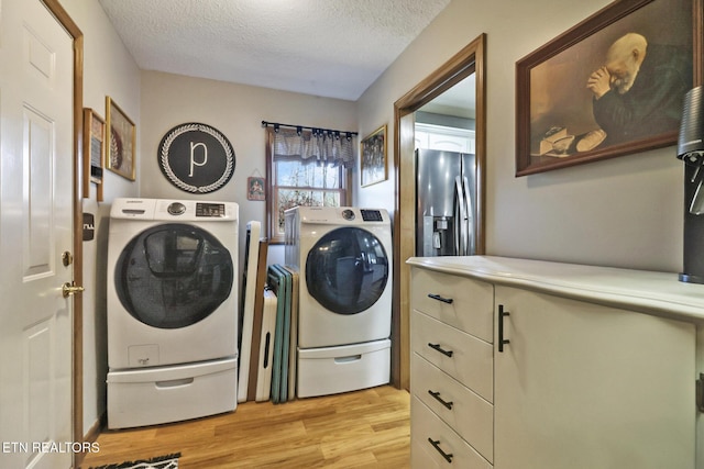 clothes washing area featuring washer and dryer, a textured ceiling, and light hardwood / wood-style flooring