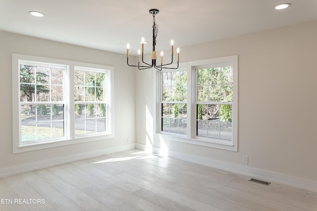 unfurnished dining area featuring a notable chandelier, a healthy amount of sunlight, and light wood-type flooring