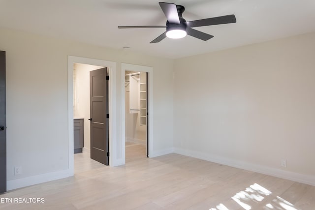 unfurnished bedroom with light hardwood / wood-style flooring, a spacious closet, a closet, and ceiling fan