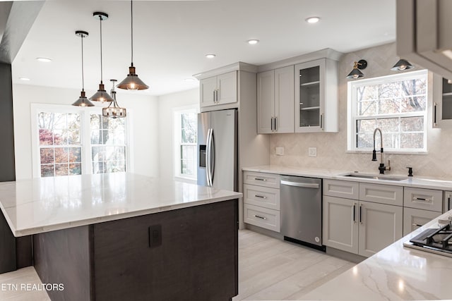 kitchen featuring pendant lighting, a center island, sink, light stone countertops, and stainless steel appliances