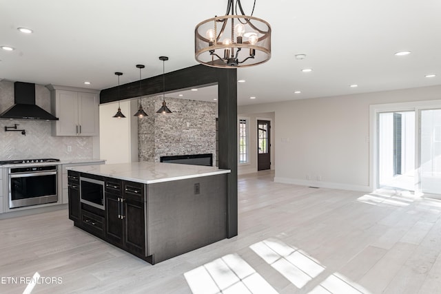 kitchen featuring pendant lighting, a center island, backsplash, wall chimney range hood, and stainless steel appliances