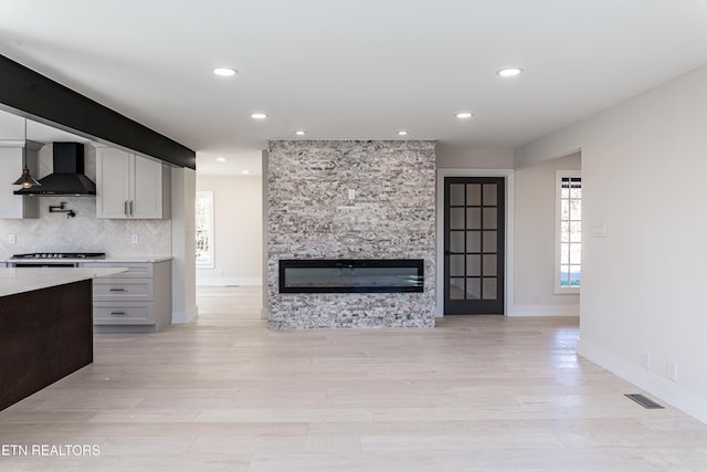 kitchen featuring wall chimney exhaust hood, backsplash, light hardwood / wood-style floors, a fireplace, and white cabinets