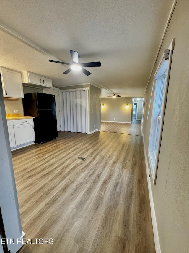 unfurnished living room with a textured ceiling, light wood-type flooring, and ceiling fan