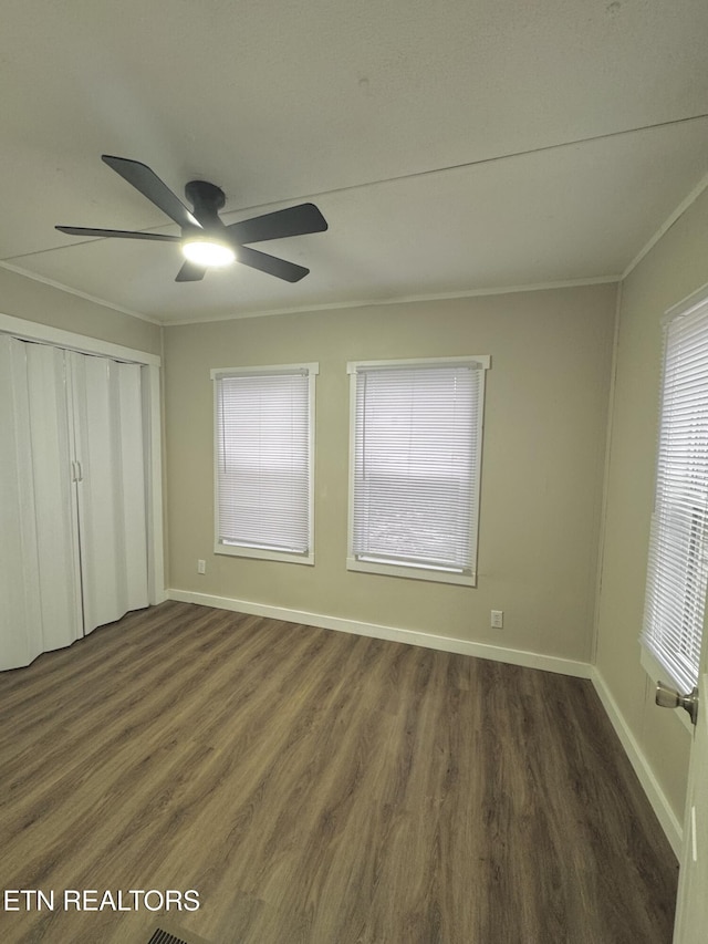 unfurnished bedroom with multiple windows, ceiling fan, crown molding, and dark wood-type flooring