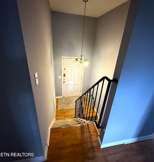 stairs with hardwood / wood-style floors, a high ceiling, and an inviting chandelier