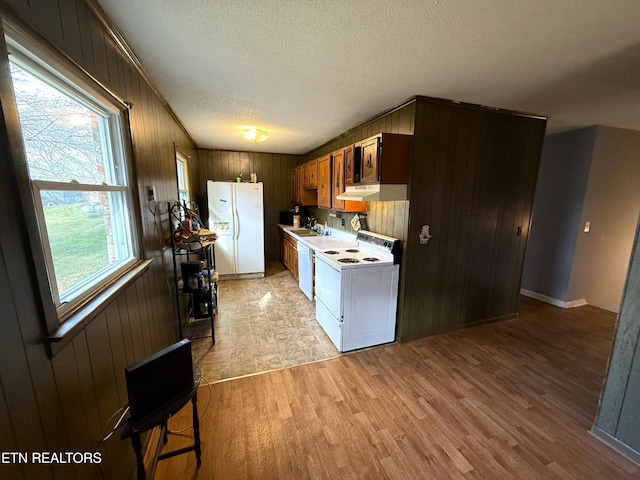 kitchen with white appliances, a textured ceiling, wooden walls, light hardwood / wood-style flooring, and washer / dryer