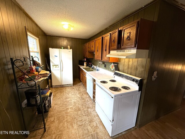 kitchen with a textured ceiling, wood walls, white appliances, and sink