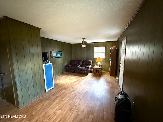 living room featuring light hardwood / wood-style flooring, ceiling fan, and wood walls