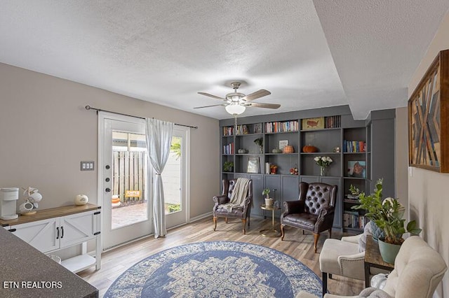 living area with ceiling fan, light hardwood / wood-style flooring, and a textured ceiling