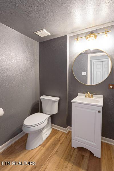 bathroom with hardwood / wood-style floors, vanity, toilet, and a textured ceiling