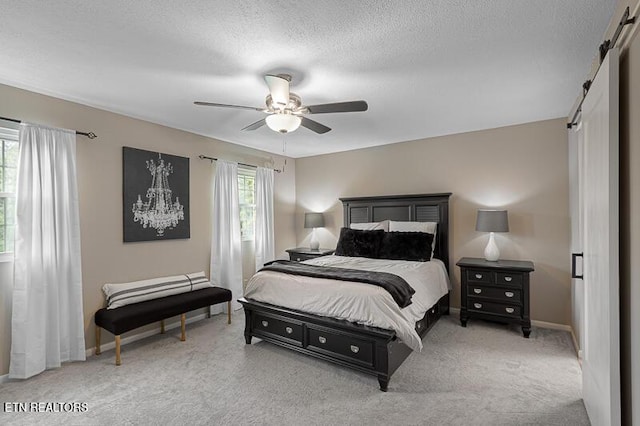 carpeted bedroom featuring a barn door, ceiling fan, and a textured ceiling