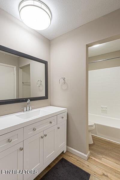 full bathroom featuring vanity, wood-type flooring, a textured ceiling, and toilet