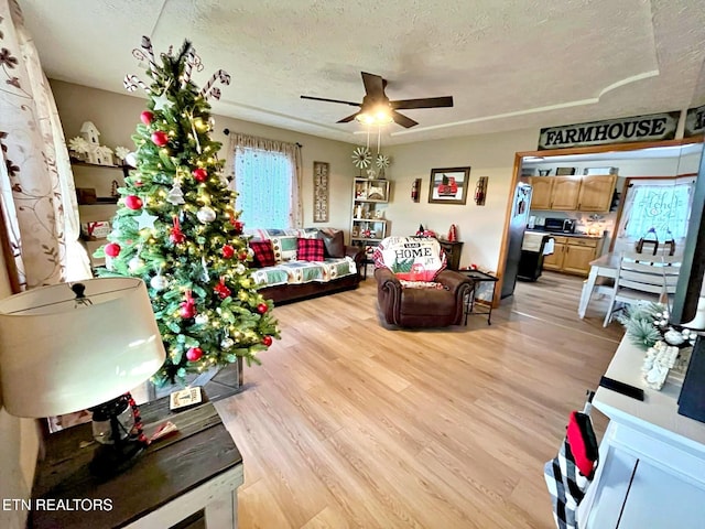 living room with ceiling fan, light wood-type flooring, and a textured ceiling