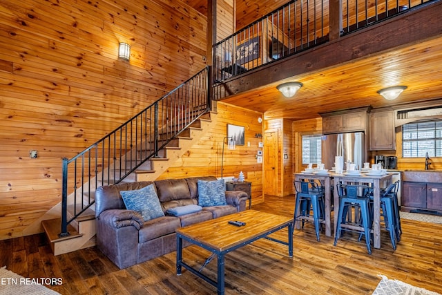 living room featuring sink, light hardwood / wood-style flooring, a towering ceiling, wooden walls, and wood ceiling