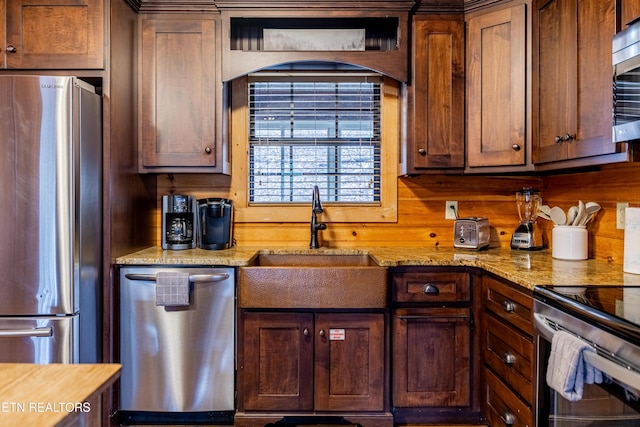 kitchen featuring wooden walls, light stone countertops, sink, and appliances with stainless steel finishes