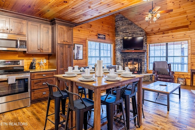 dining room with light wood-type flooring, ceiling fan, wooden ceiling, a stone fireplace, and lofted ceiling