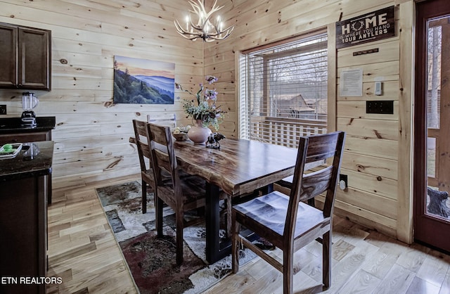 dining room featuring light hardwood / wood-style flooring, a notable chandelier, and wooden walls