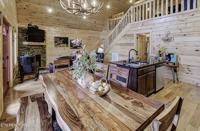 dining space featuring a fireplace, a notable chandelier, sink, light wood-type flooring, and wooden ceiling