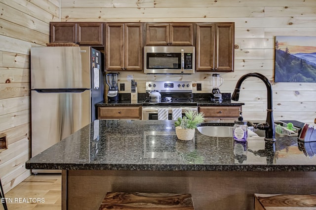 kitchen featuring dark stone countertops, wood walls, and stainless steel appliances