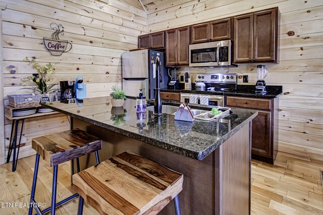 kitchen featuring dark brown cabinetry, appliances with stainless steel finishes, a breakfast bar area, and light hardwood / wood-style floors