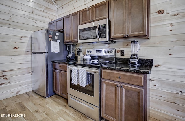 kitchen featuring light wood-type flooring, stainless steel appliances, and wooden walls