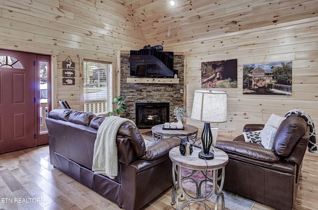 living room featuring wooden walls, light hardwood / wood-style flooring, wood ceiling, a stone fireplace, and high vaulted ceiling