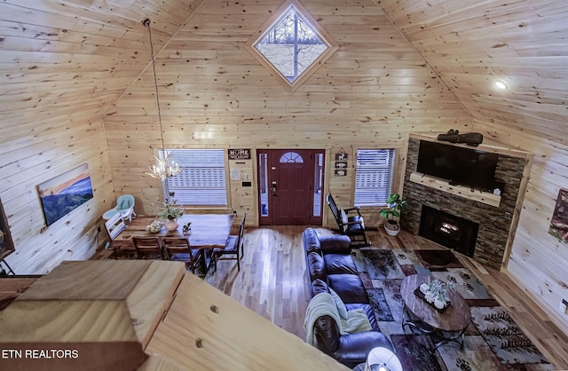 living room featuring lofted ceiling, wood ceiling, wood-type flooring, a stone fireplace, and wooden walls