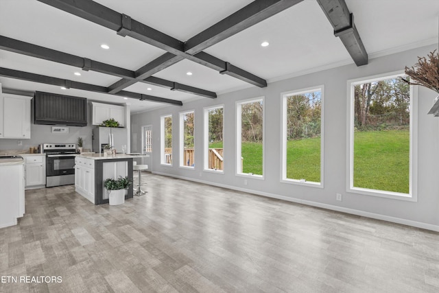 kitchen featuring beam ceiling, a kitchen breakfast bar, stainless steel electric range, a center island with sink, and white cabinets