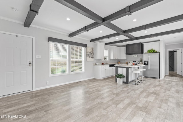 kitchen with beam ceiling, a center island, stainless steel fridge, a breakfast bar, and white cabinets