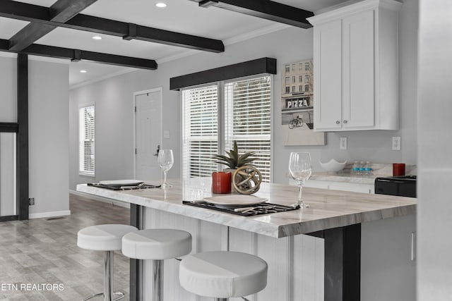 kitchen with light stone countertops, a breakfast bar, white cabinets, and beamed ceiling