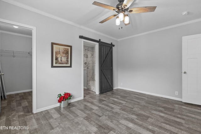 unfurnished bedroom with ceiling fan, a spacious closet, dark wood-type flooring, a barn door, and crown molding