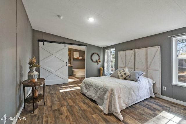 bedroom featuring a barn door, dark hardwood / wood-style floors, ensuite bath, and multiple windows