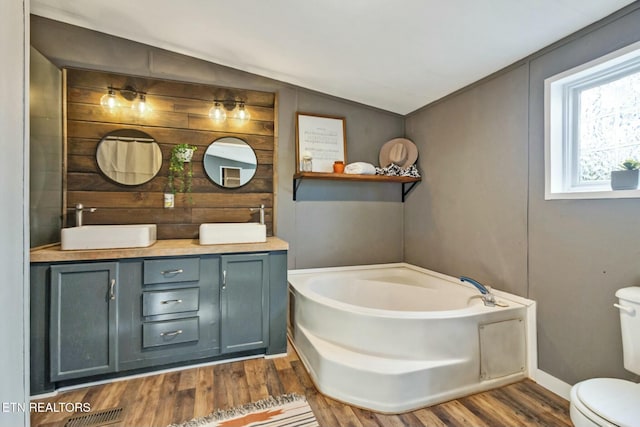 bathroom with vanity, hardwood / wood-style floors, lofted ceiling, toilet, and a tub