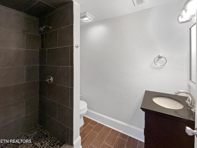 bathroom with a tile shower, vanity, and toilet