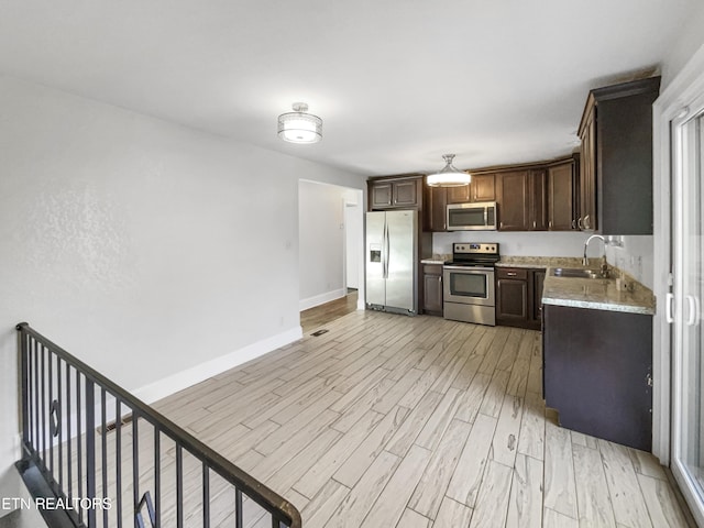 kitchen featuring appliances with stainless steel finishes, light wood-type flooring, light stone counters, dark brown cabinetry, and sink