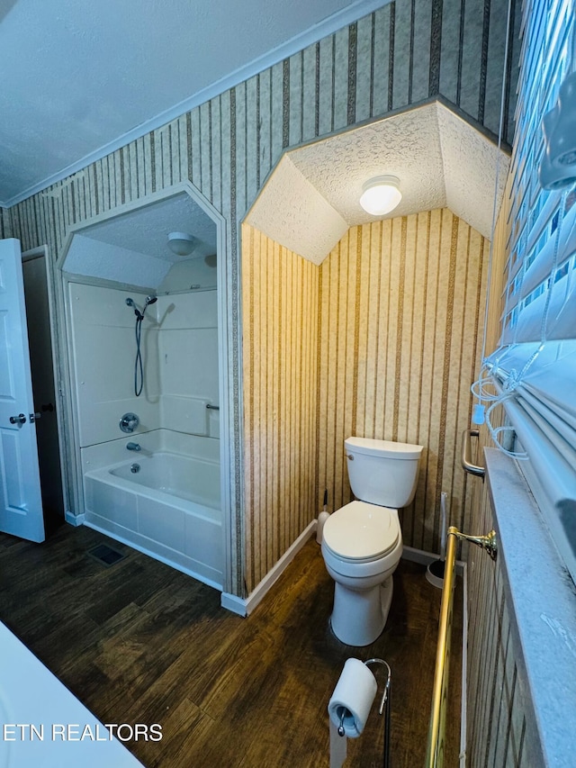 bathroom featuring bathing tub / shower combination, hardwood / wood-style floors, a textured ceiling, lofted ceiling, and toilet