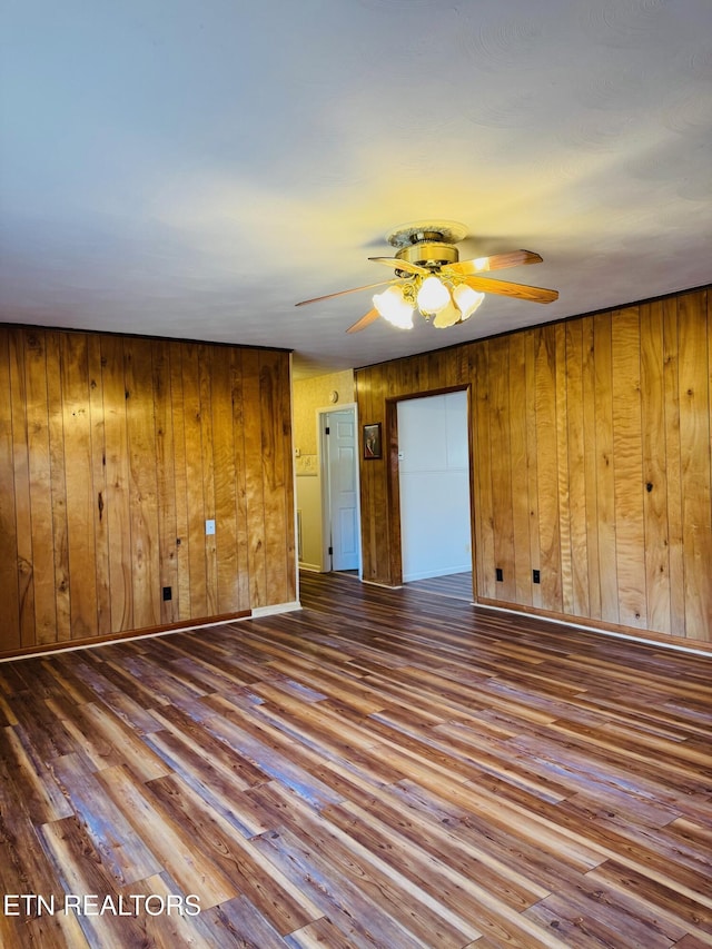 unfurnished room with wood-type flooring, ceiling fan, and wood walls