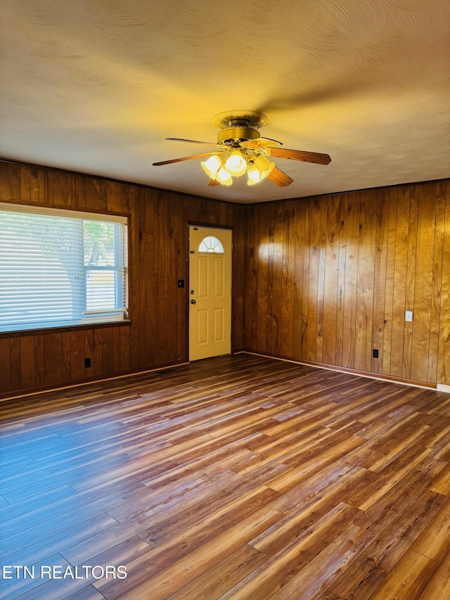 interior space with ceiling fan, wood-type flooring, and wooden walls