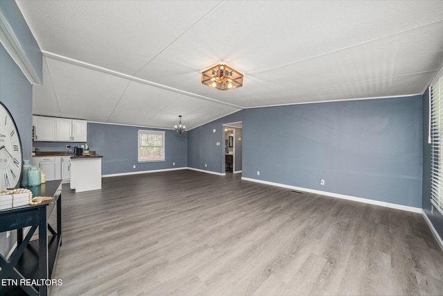 unfurnished living room with a notable chandelier, light hardwood / wood-style floors, and vaulted ceiling