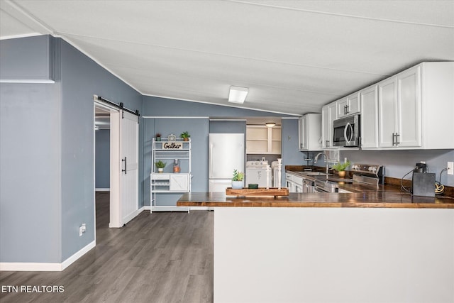 kitchen with lofted ceiling, white cabinets, a barn door, kitchen peninsula, and stainless steel appliances