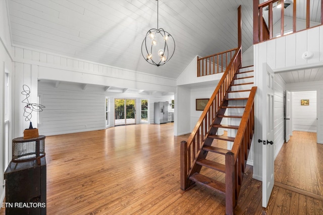 living room with wooden walls, an inviting chandelier, high vaulted ceiling, and light wood-type flooring