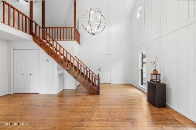 entrance foyer featuring an inviting chandelier, light hardwood / wood-style flooring, high vaulted ceiling, and wooden walls