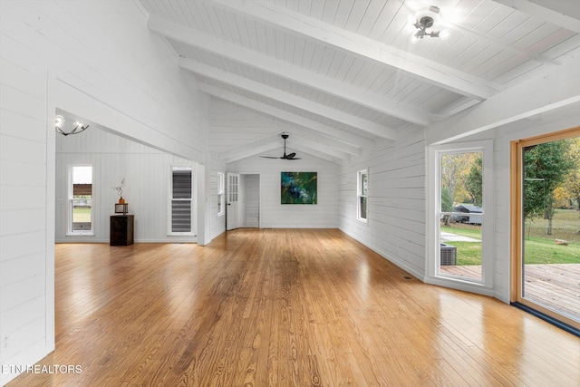 unfurnished living room featuring vaulted ceiling with beams, wood walls, light hardwood / wood-style floors, and ceiling fan with notable chandelier