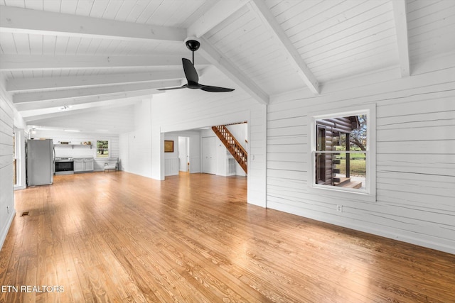 unfurnished living room with ceiling fan, vaulted ceiling with beams, light hardwood / wood-style floors, and wooden walls