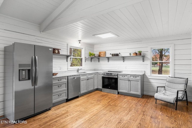 kitchen featuring beamed ceiling, light wood-type flooring, stainless steel appliances, and a healthy amount of sunlight